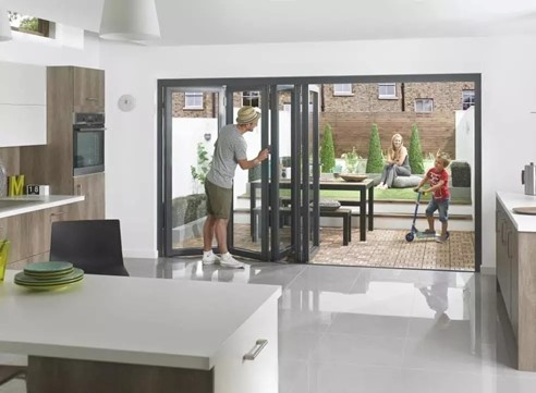 Large Aluminium bifold doors being opened by a father of a family who are out playing in the garden